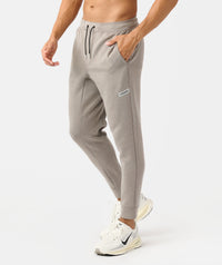 Taupe heather joggers with drawstring waist, side pockets, and tapered ankles on male model wearing white sneakers.