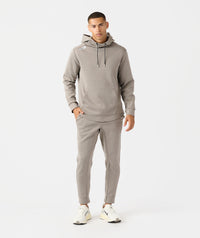 Man wearing taupe heather hoodie and matching joggers with drawstring waist and cuffed ankles.