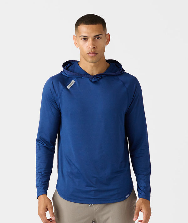 Man wearing a blue long-sleeve hooded shirt with a small chest label, paired with khaki pants.