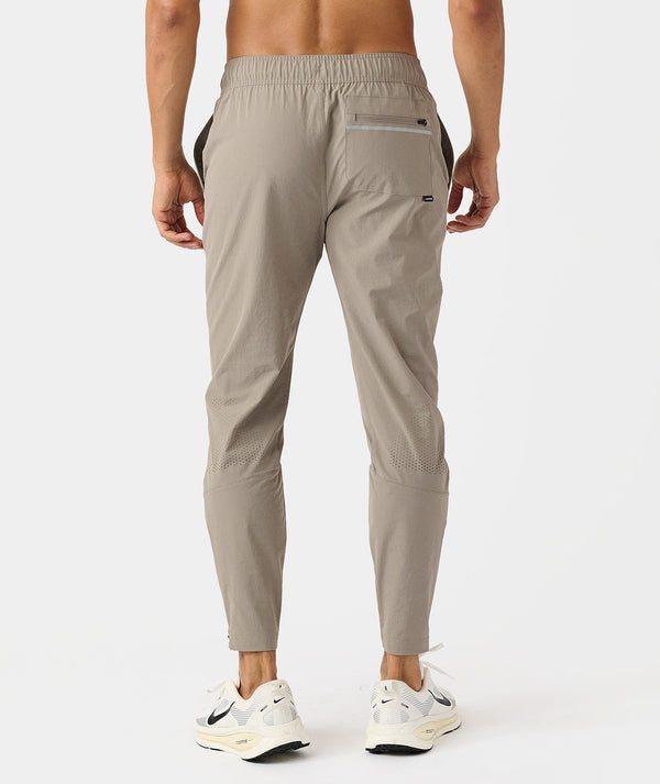 Taupe jogger pants with elastic waistband, zip pockets, and mesh paneling on legs, shown from back view.