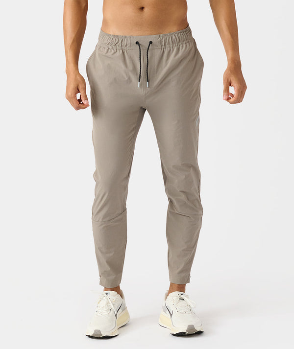Taupe jogger pants with drawstring waistband and tapered ankles, worn with white sneakers.