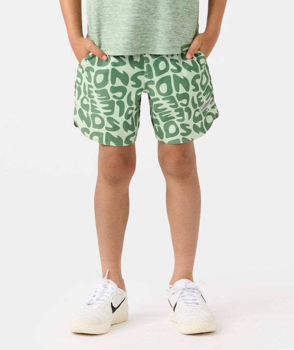 Child wearing green patterned shorts with abstract lettering design and white sneakers.