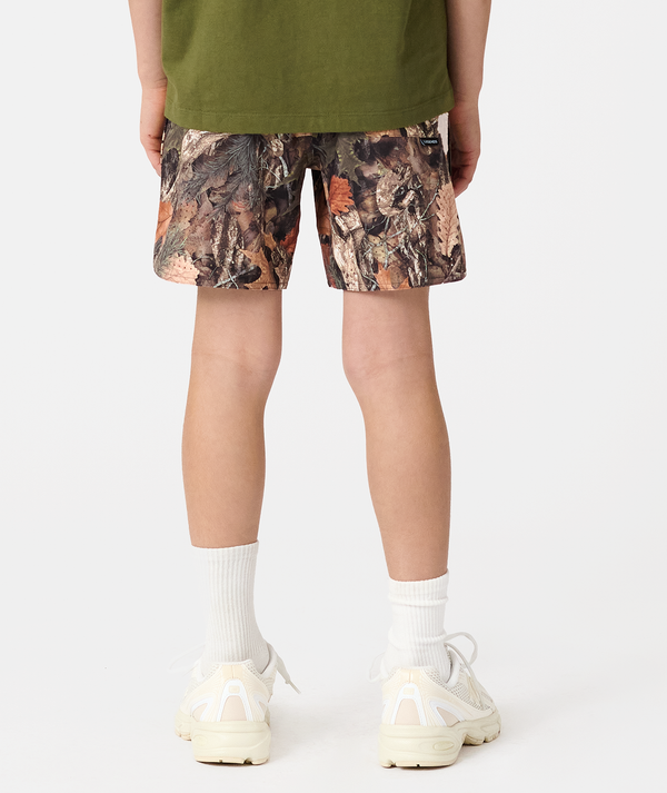 Child wearing forest camouflage shorts with olive green shirt, white socks, and cream sneakers.