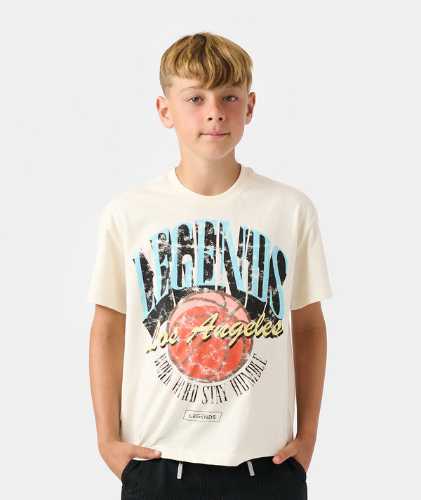 Child wearing natural white short-sleeve t-shirt with "Vagabonds Los Angeles" graphic print and red circle design on chest.