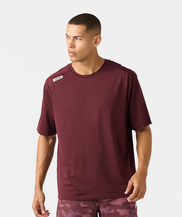 Burgundy crew neck t-shirt with small label patch on chest, worn by male model.