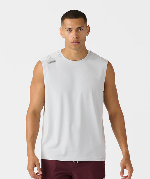 White sleeveless tank top with small gray brand label on shoulder, worn with burgundy pants.
