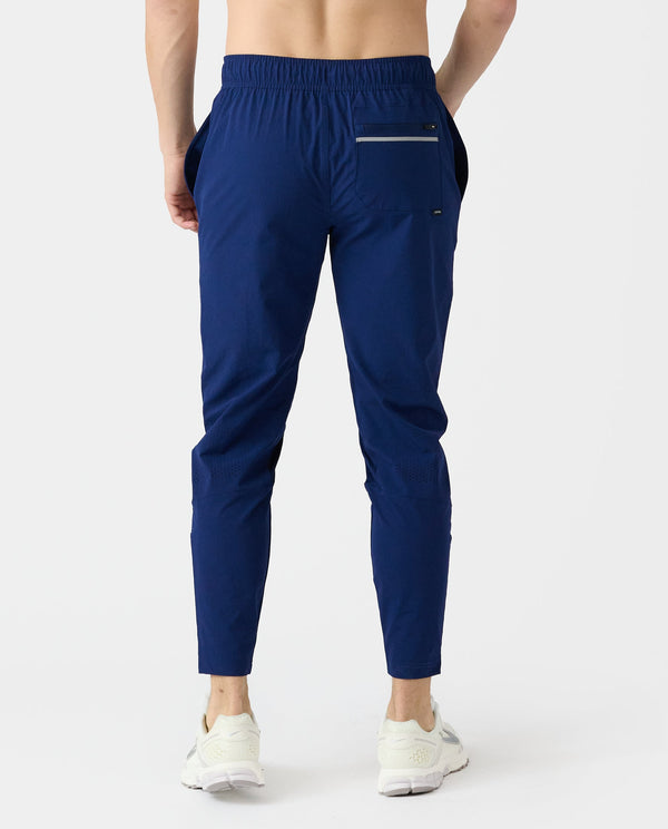 Navy blue jogger pants with elastic waistband, back pocket, and tapered ankle cuffs, shown on model from waist down.