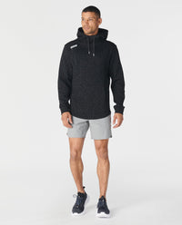 Black speckled hoodie with white drawstring worn with gray shorts and black sneakers.