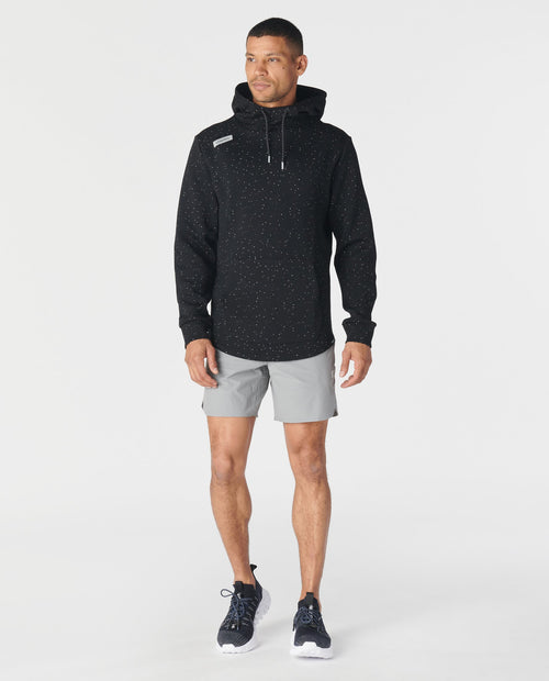 Black speckled hoodie with white drawstring worn with gray shorts and black sneakers.