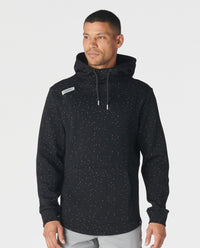 Black hoodie with white speckled splatter pattern throughout, drawstring hood, and brand label on chest.