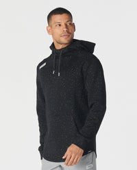 Black hoodie with white speckled splatter pattern throughout, drawstring hood, and small chest logo patch.