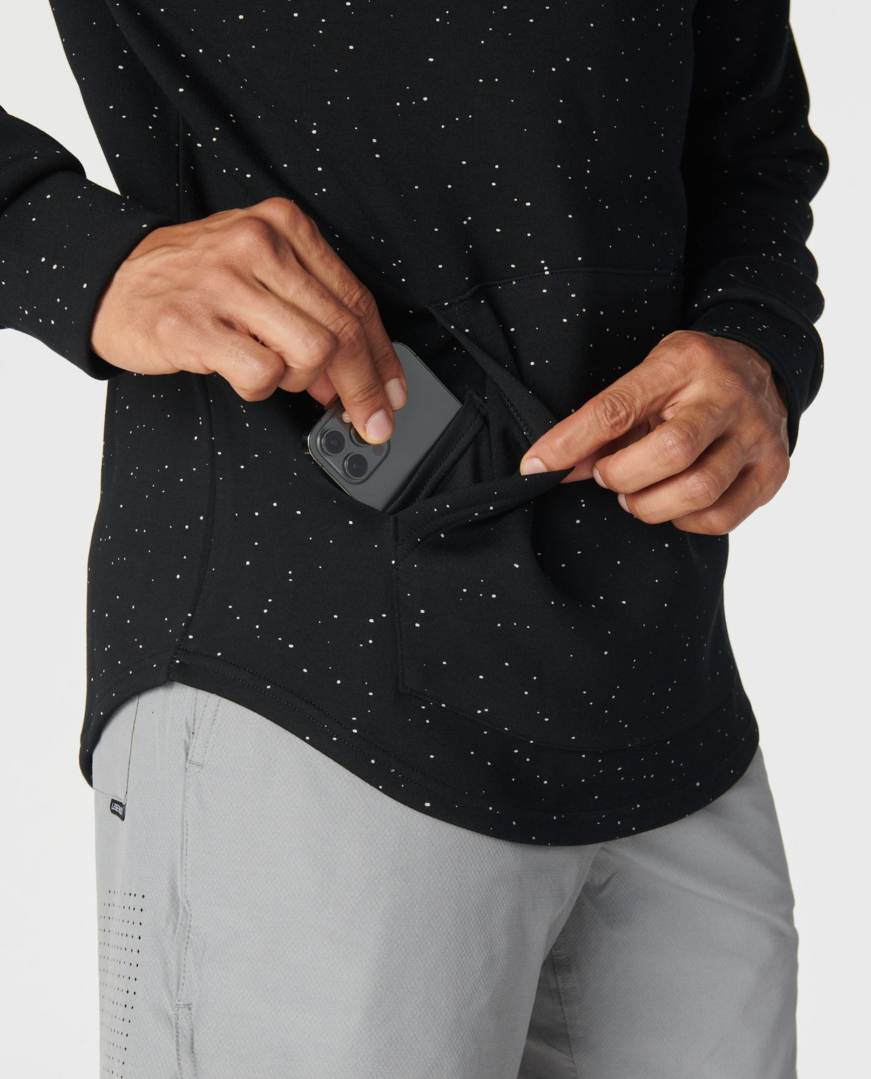 Black hoodie with white speckled pattern, front kangaroo pocket, worn with gray pants.